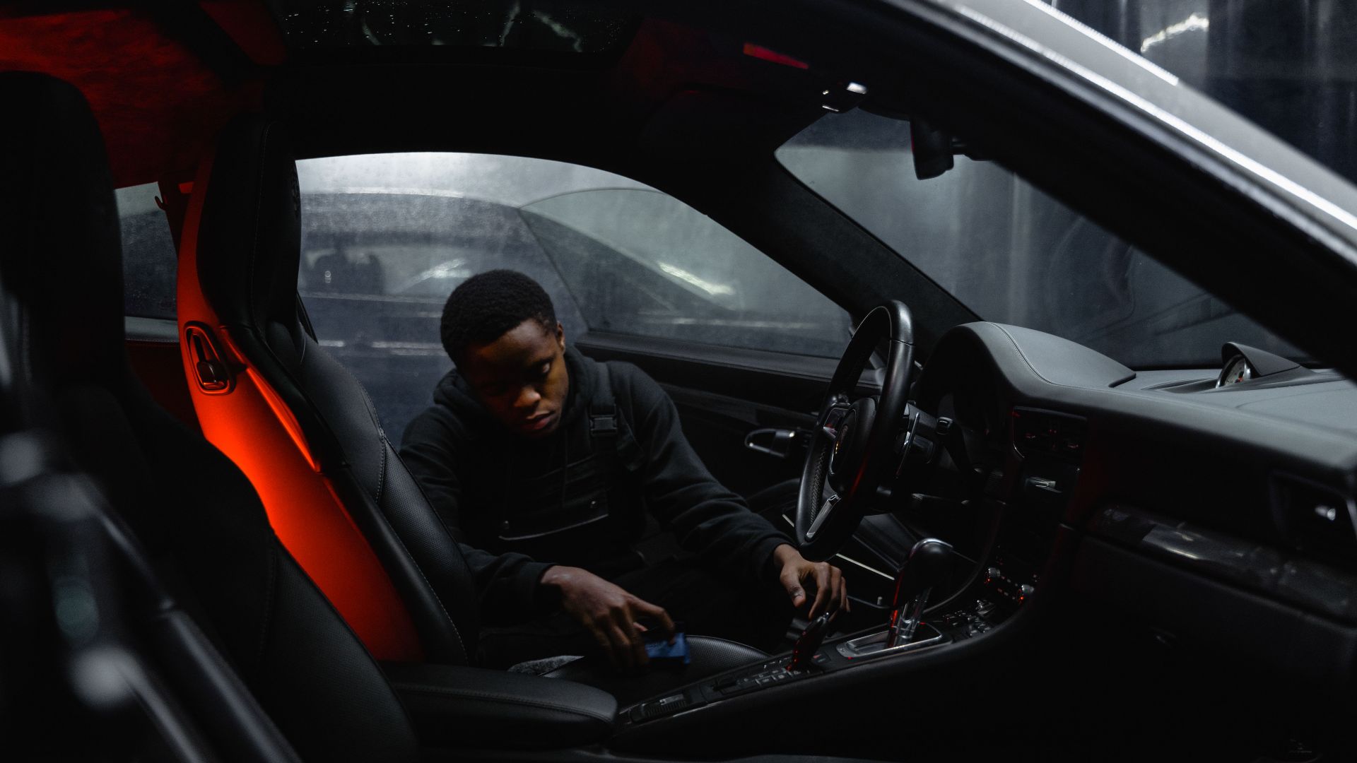A man carefully cleaning the interior of a car at night, focusing on detailing.
