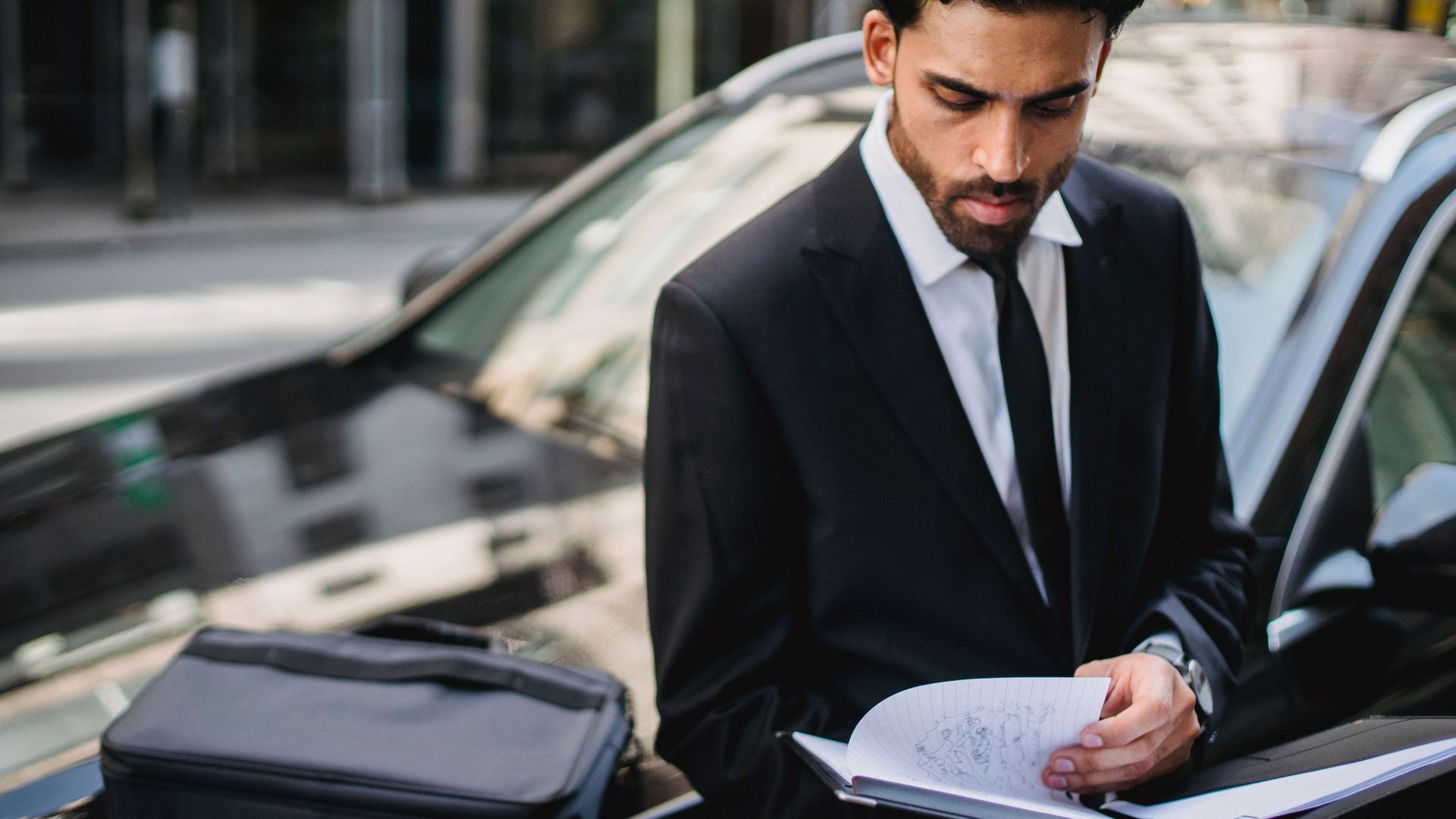 Confident businessman reviewing documents on the street beside a car.