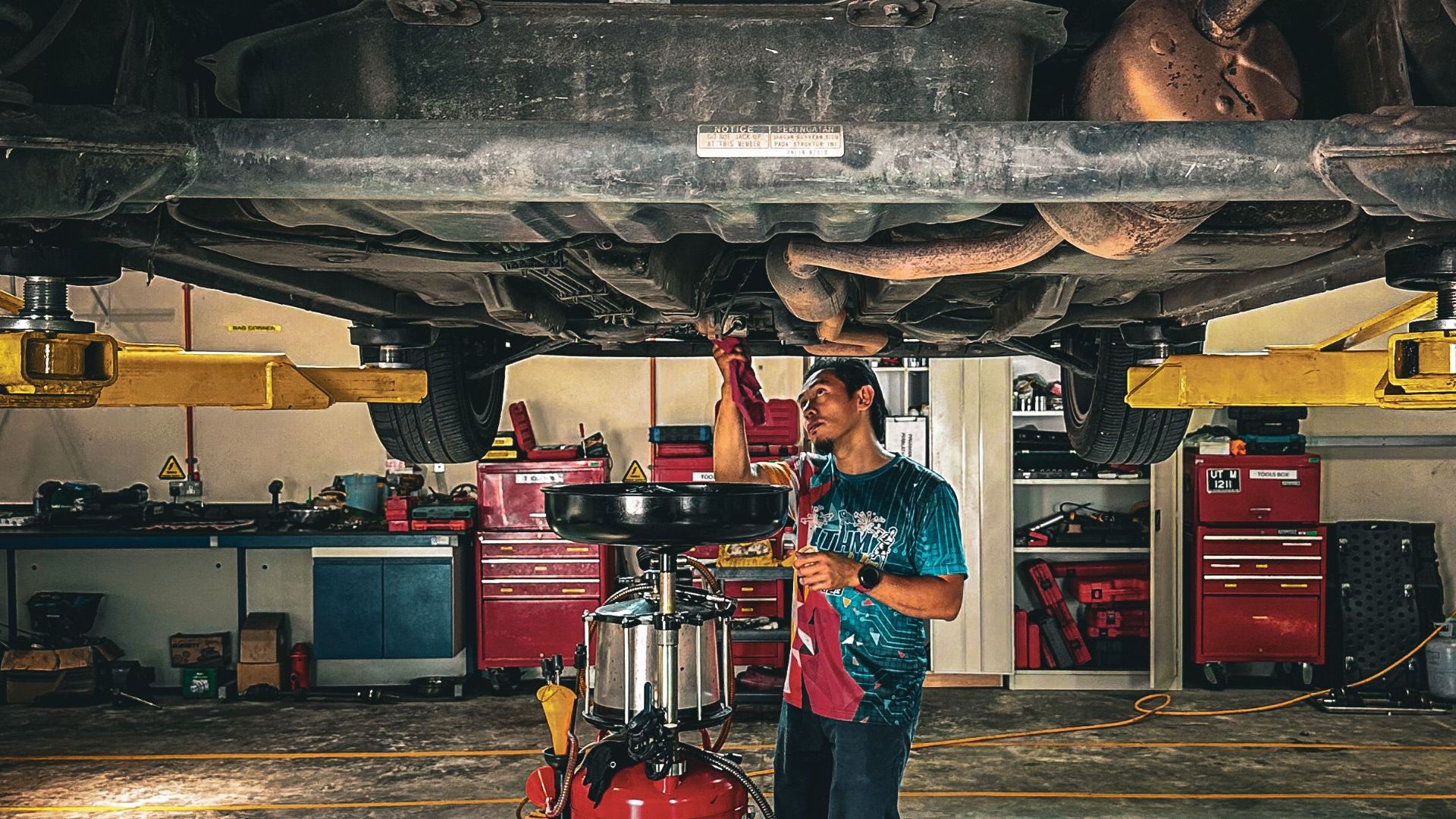 Mechanic inspecting car underside in a professional garage setup.