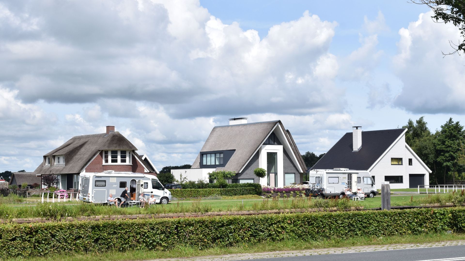 Empty asphalt road with fence and row of country houses under blue sky with clouds