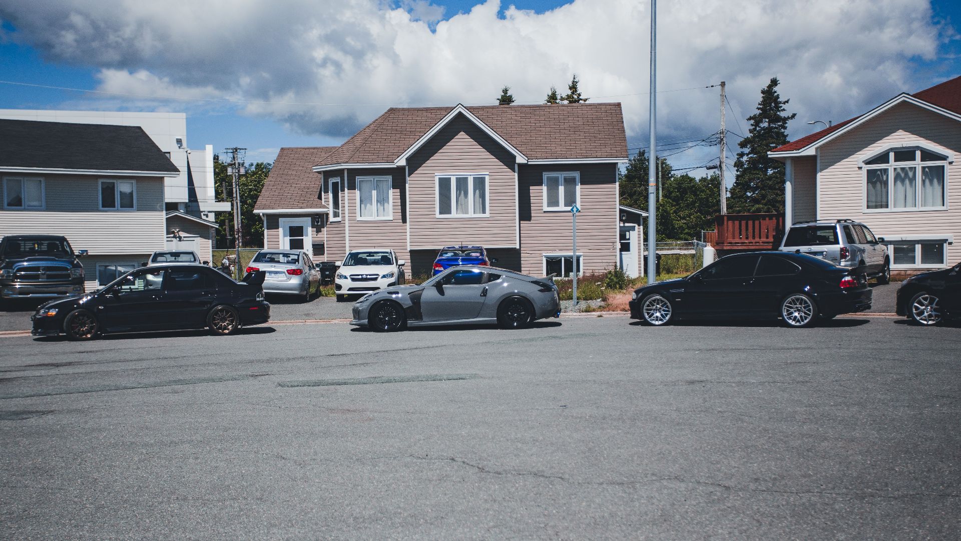 Sunny neighborhood street with modern homes and parked vehicles on a bright day.
