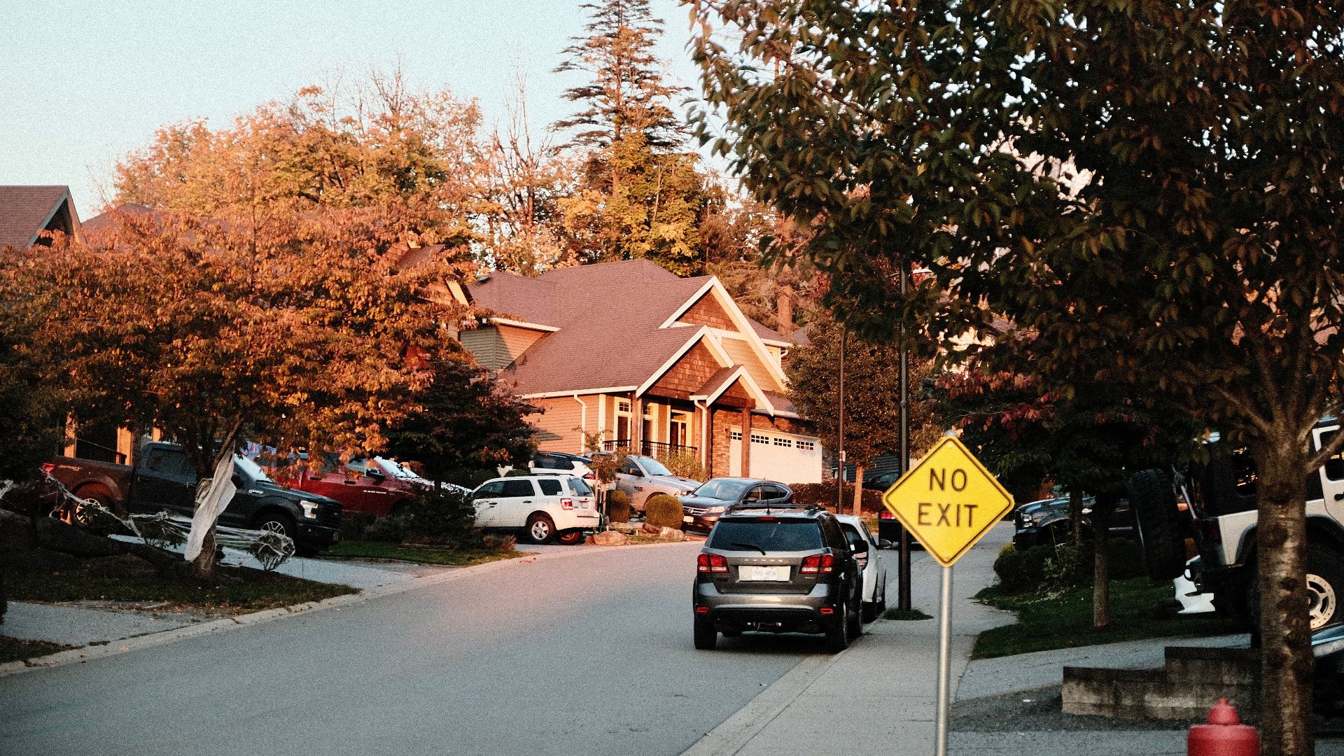 Charming suburban street scene with houses, cars, and a no exit sign in fall.