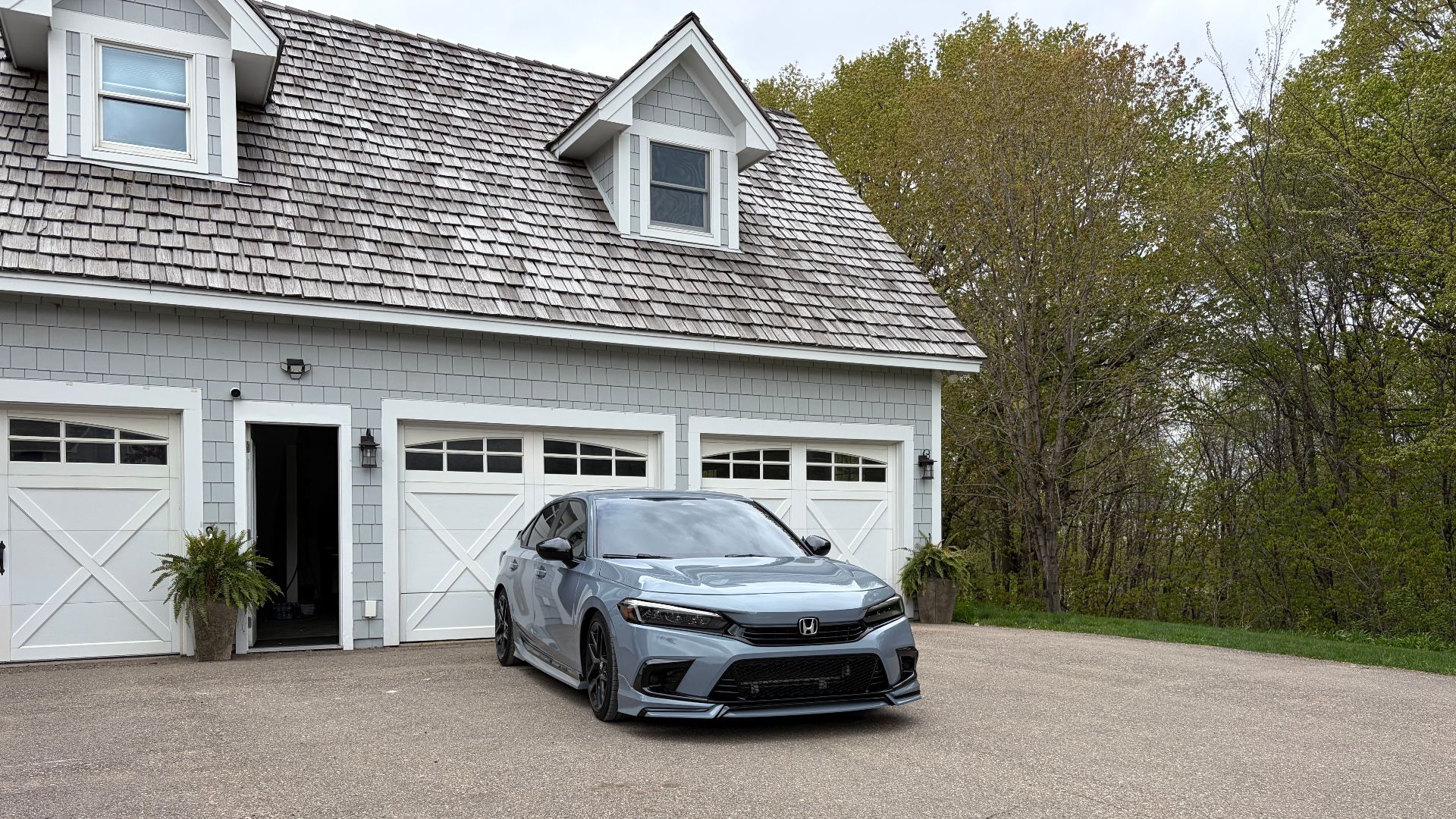 Modern gray sedan parked in front of a suburban three-car garage with lush greenery.