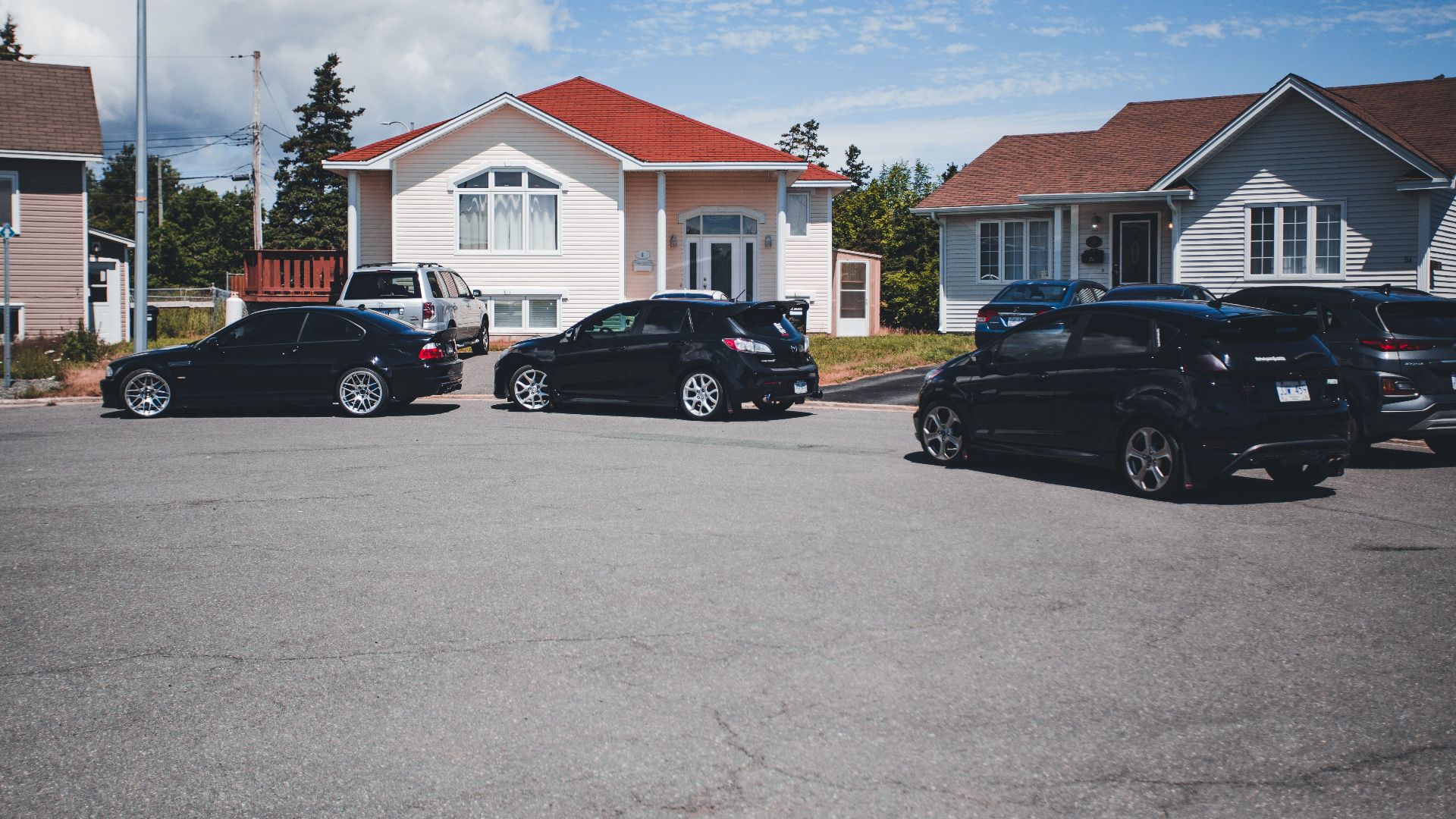 A quiet suburban street with parked cars in front of modern houses under a clear blue sky.