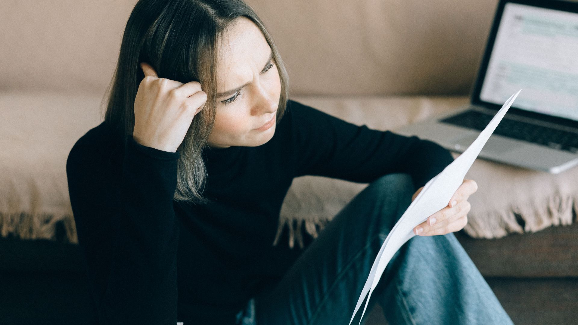 Focused woman analyzing papers with a laptop open, symbolizing thoughtful consideration.