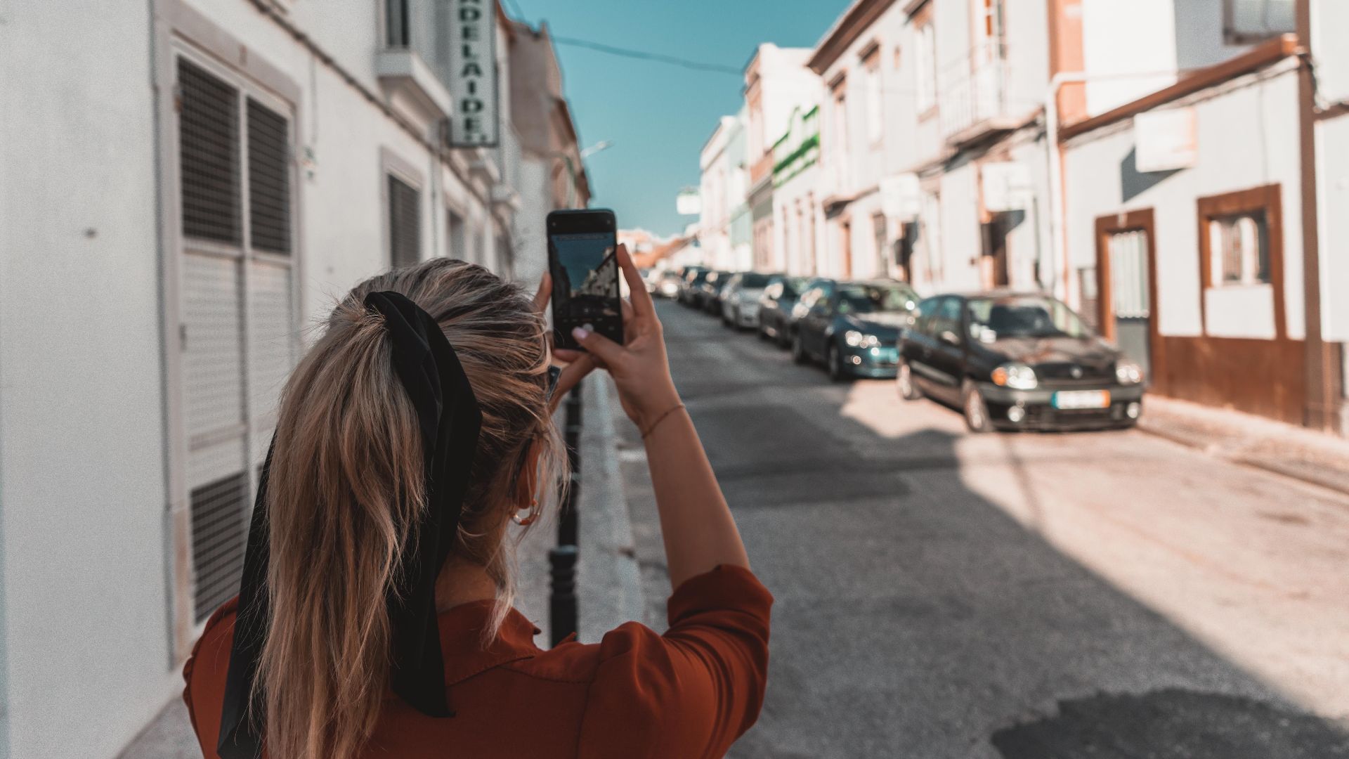 Woman capturing a European street with her smartphone on a sunny day.