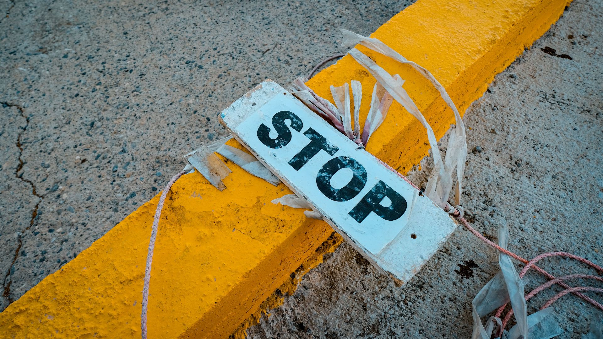 A worn 'STOP' sign placed on a cracked concrete pavement next to a yellow curb.