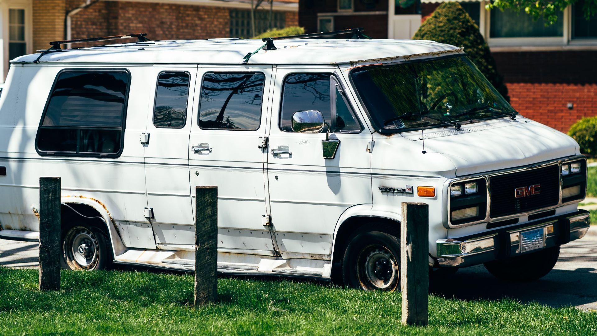 Old white van parked outdoors in a green suburban setting on a sunny day.