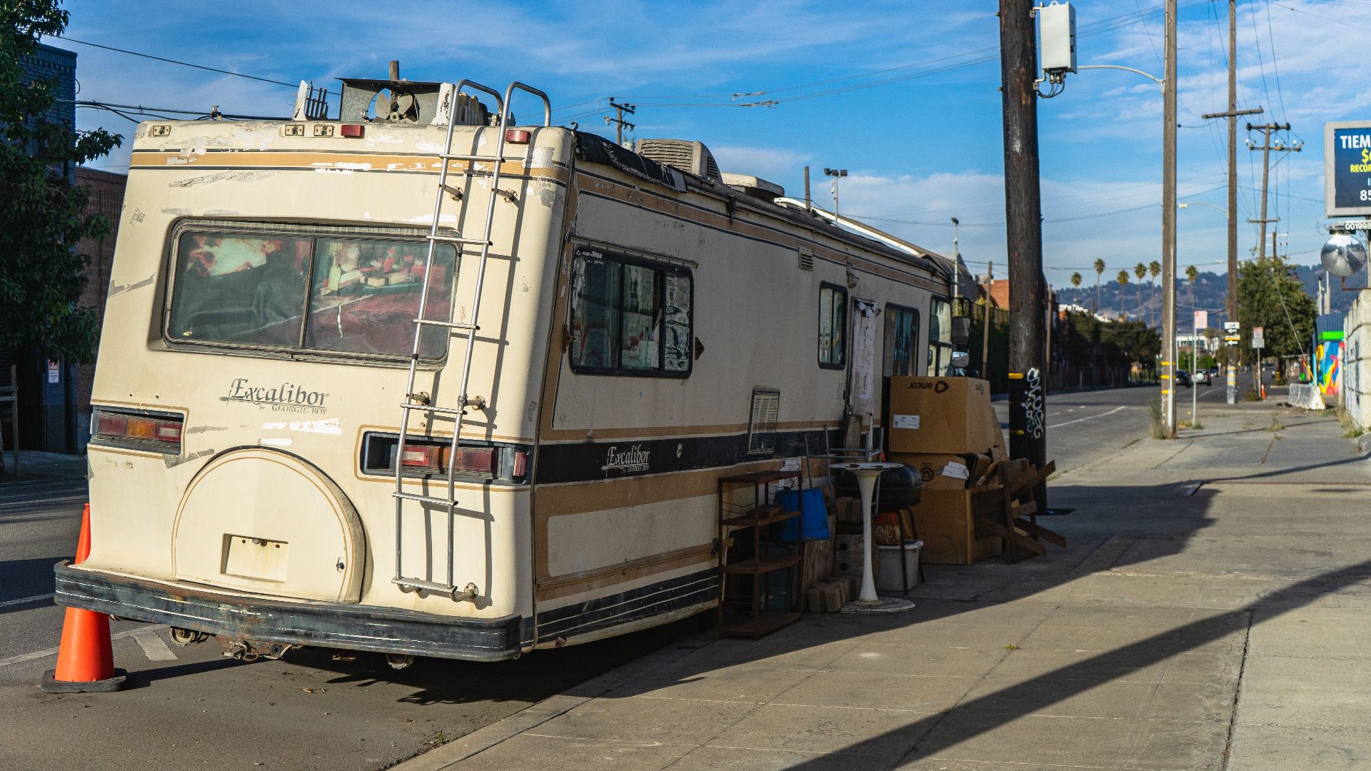 A vintage Excalibur RV parked on an urban street with scattered items outside.