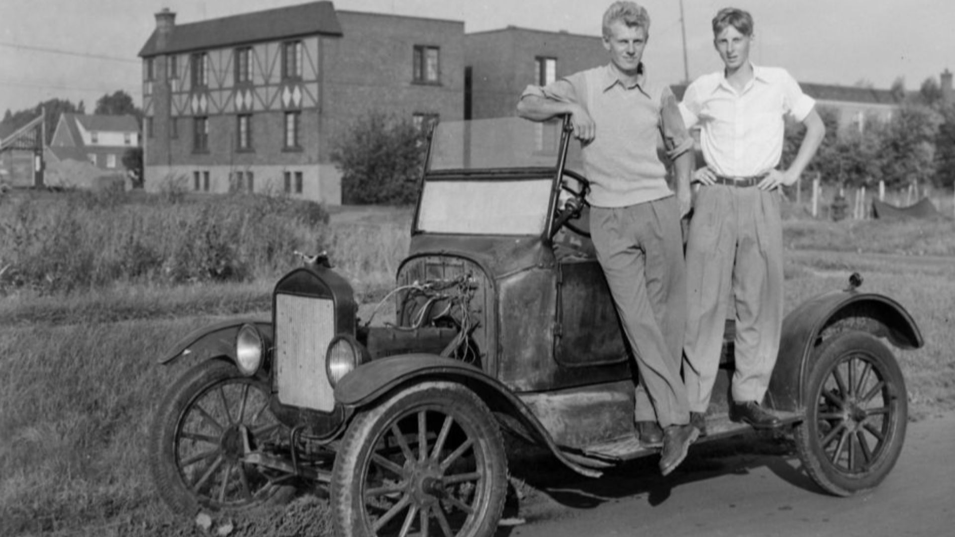 Two young men stand on the running board of a car Ford 1923.