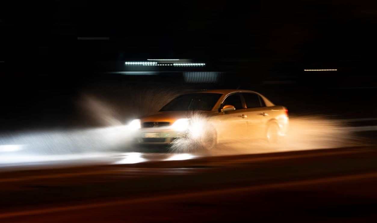 A car speeding through a wet road with dramatic splashes during a nighttime drive