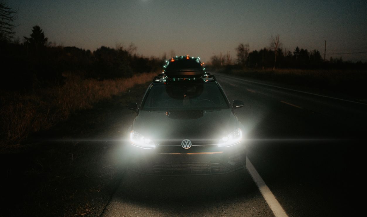 A car travels on a dark, rural road at night, illuminated by full moonlight