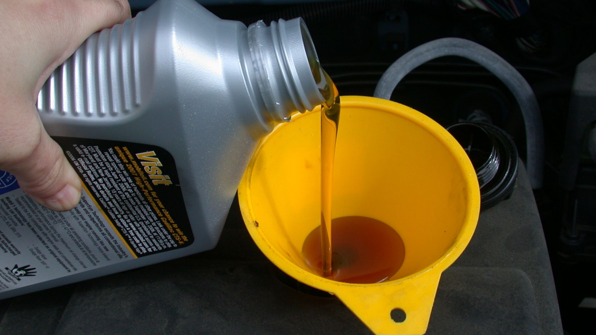 Using a funnel to refill the motor oil in an automobile as part of an oil change.