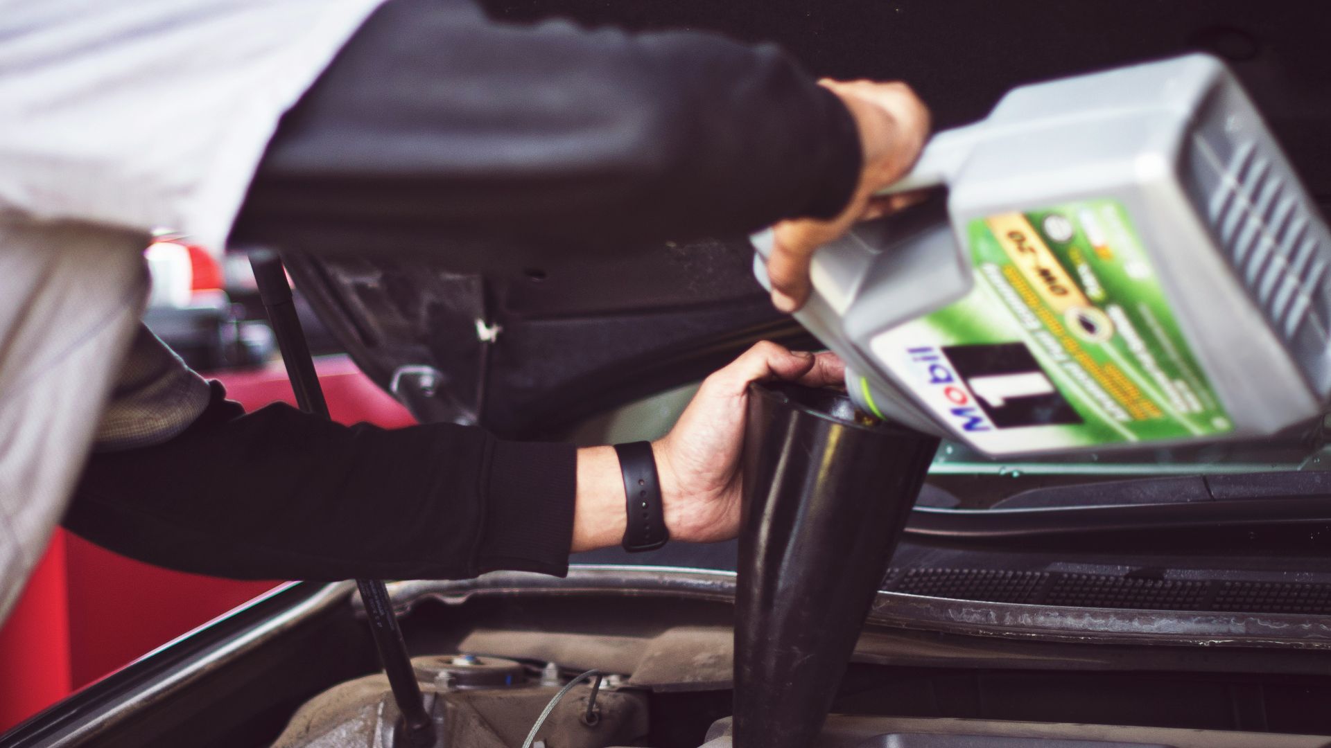 man refilling motor oil on car engine bay