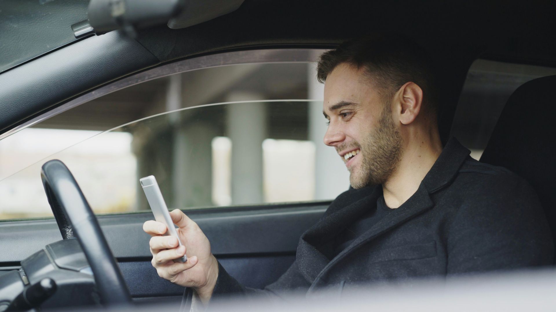 Man smiling while looking at his phone in car