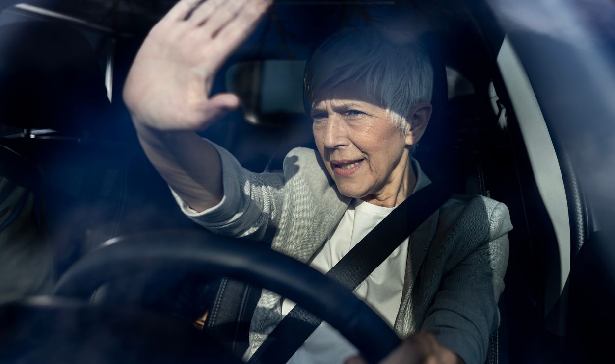 Senior woman driving car at night and is being blinded from headligts od approaching vehicle so she holding hand as shade from glare