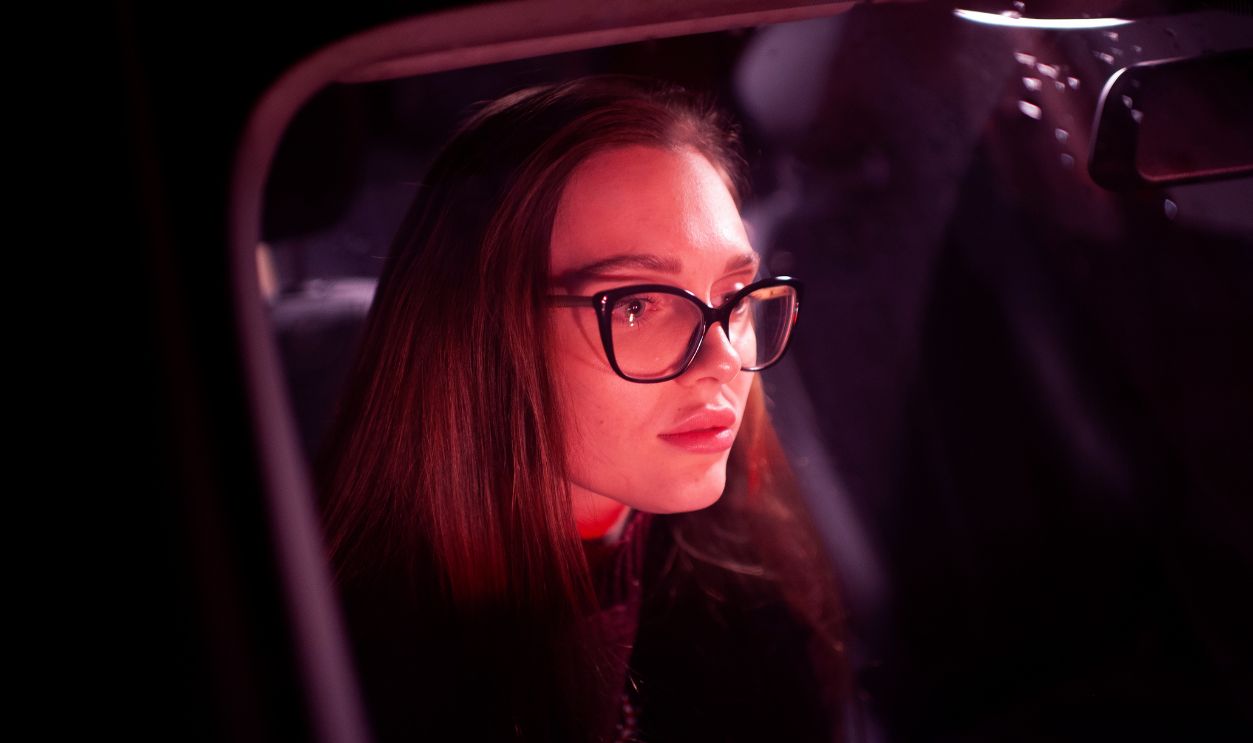 beautiful girl in glasses in red from car headlights driving a car tired in traffic in the evening. Fashion and beauty concept