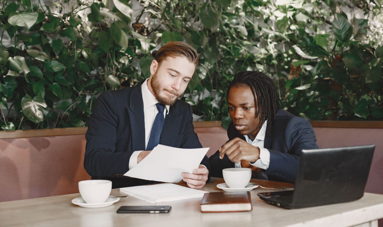 Two businessmen in a cafe discussing documents over coffee with a laptop