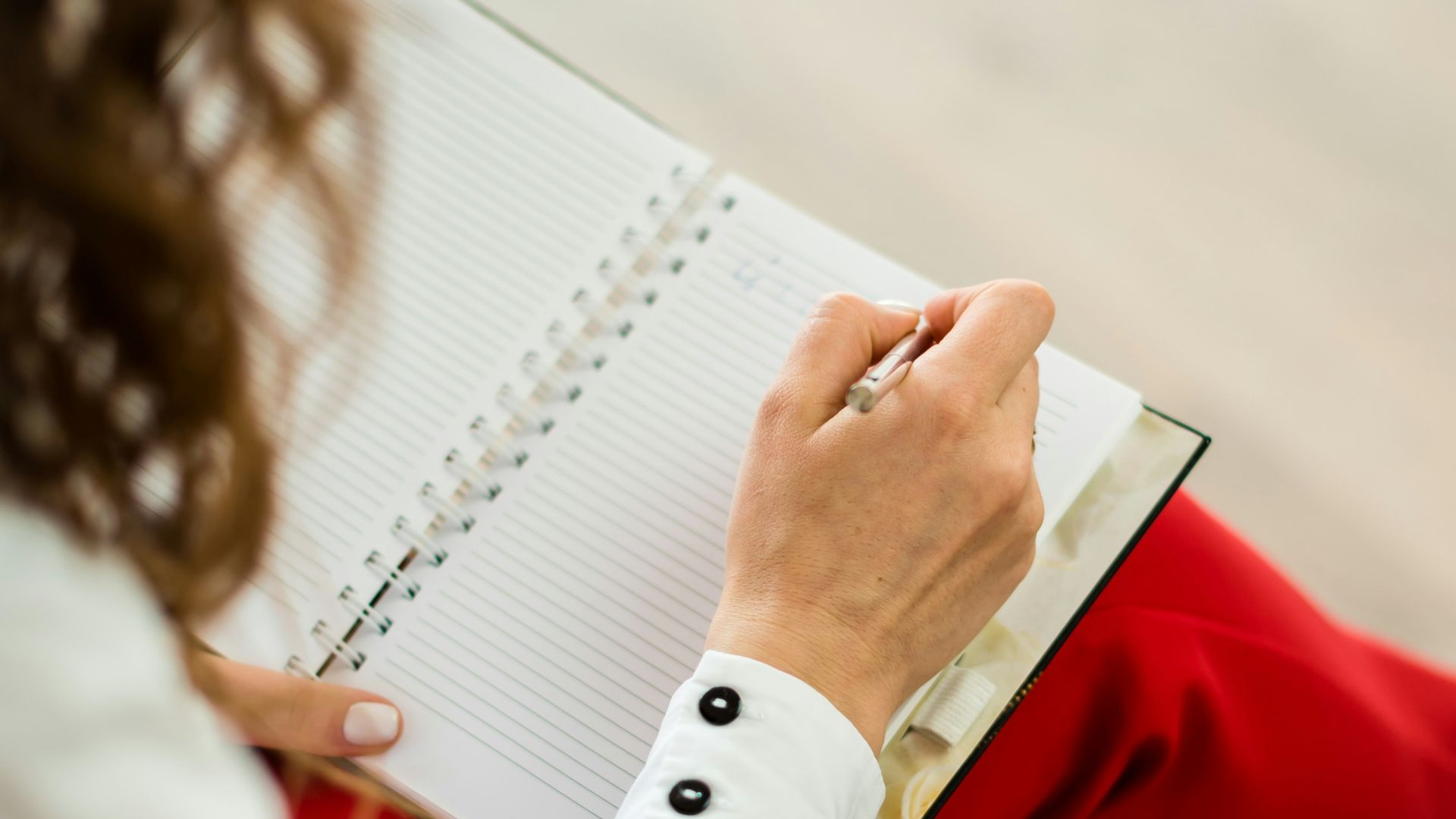 A woman in a white shirt and red trousers writing in a notebook