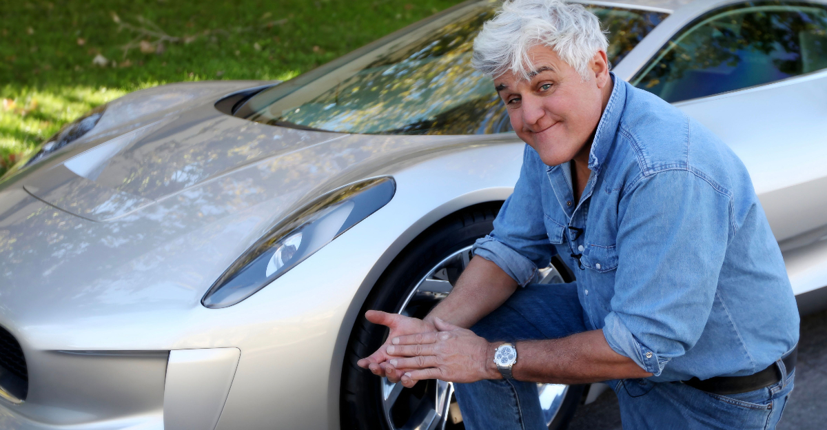 Jay Leno kneels next to a Jaguar C-X75 hybrid