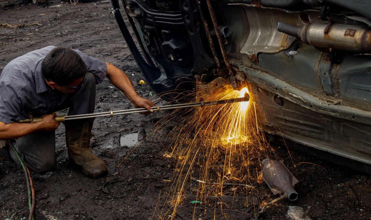 Mechanic welding a car frame outdoors, producing dramatic sparks and intense focus.