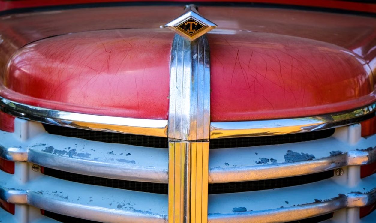 Detailed view of a scratched red and chrome vintage car hood, showcasing retro design elements.