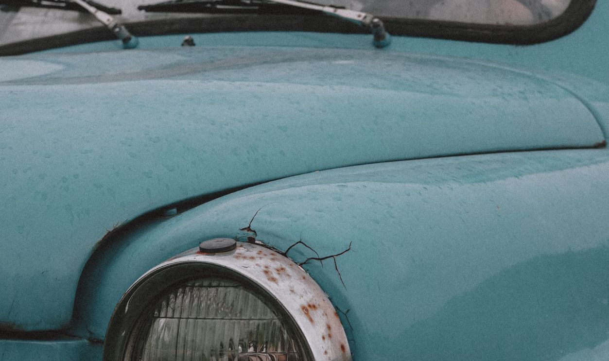Rustic close-up of a vintage blue car with raindrops and visible rust.