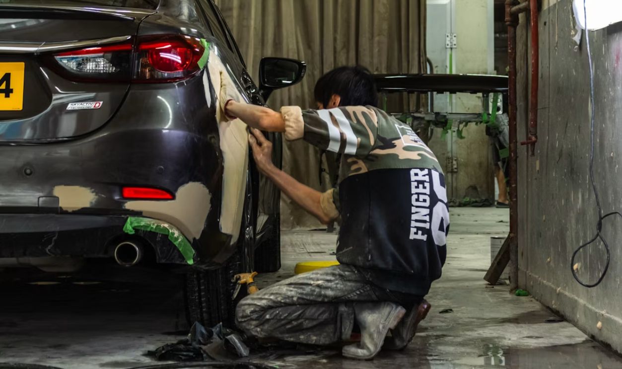 A person sanding the rear panel of a grey car in a workshop
