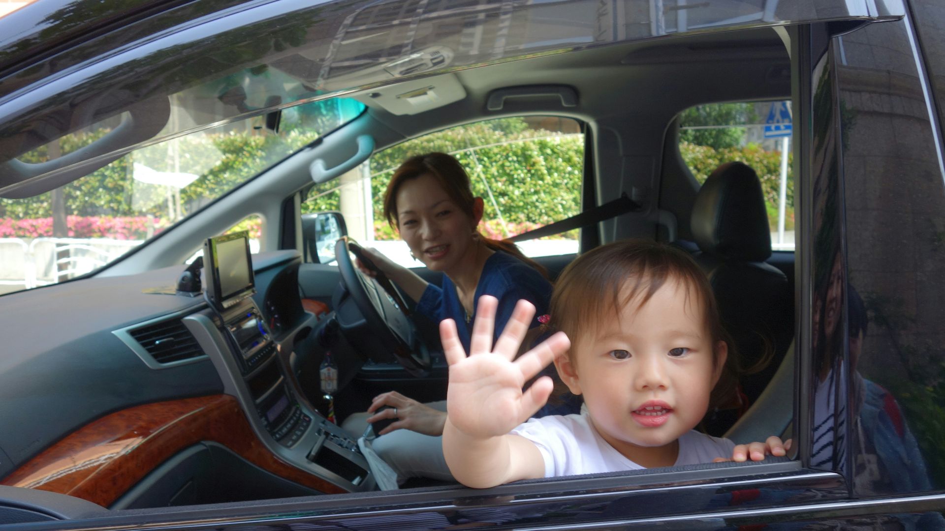 Child waves from car window with mother driving