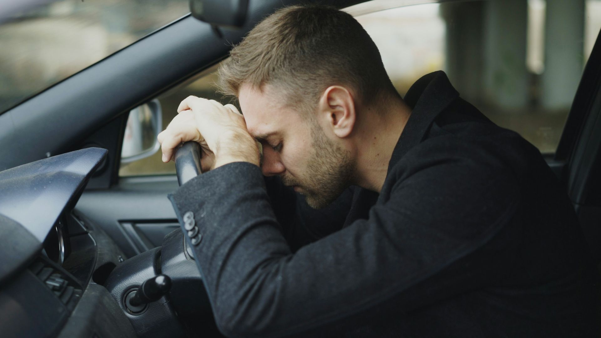 Man resting head on steering wheel in car