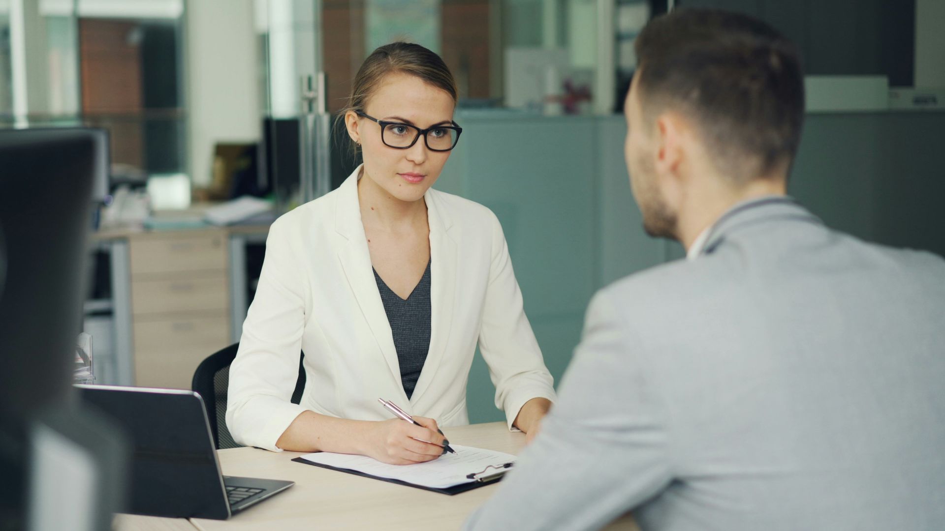 Woman in glasses interviews man at office desk