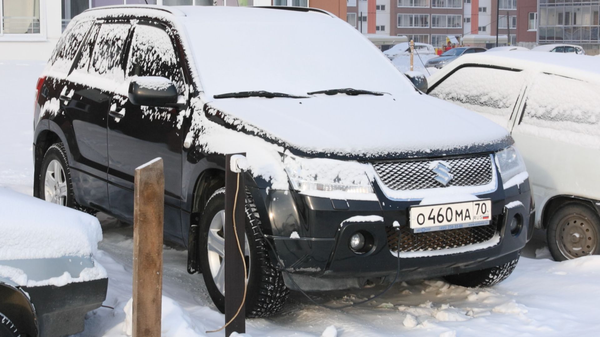 Suzuki Grand Vitara connected to electricity to power block heater. Temporary power outlet is installed by the car owner at a public parking lot with the wire coming out of his apartment window. Picture taken in Tomsk, Russia.