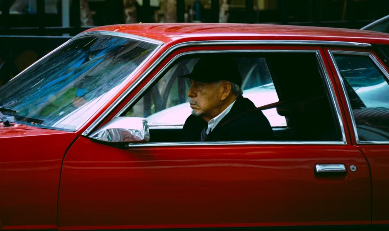 Elderly man driving a vintage red car through the streets of Callao, Lima