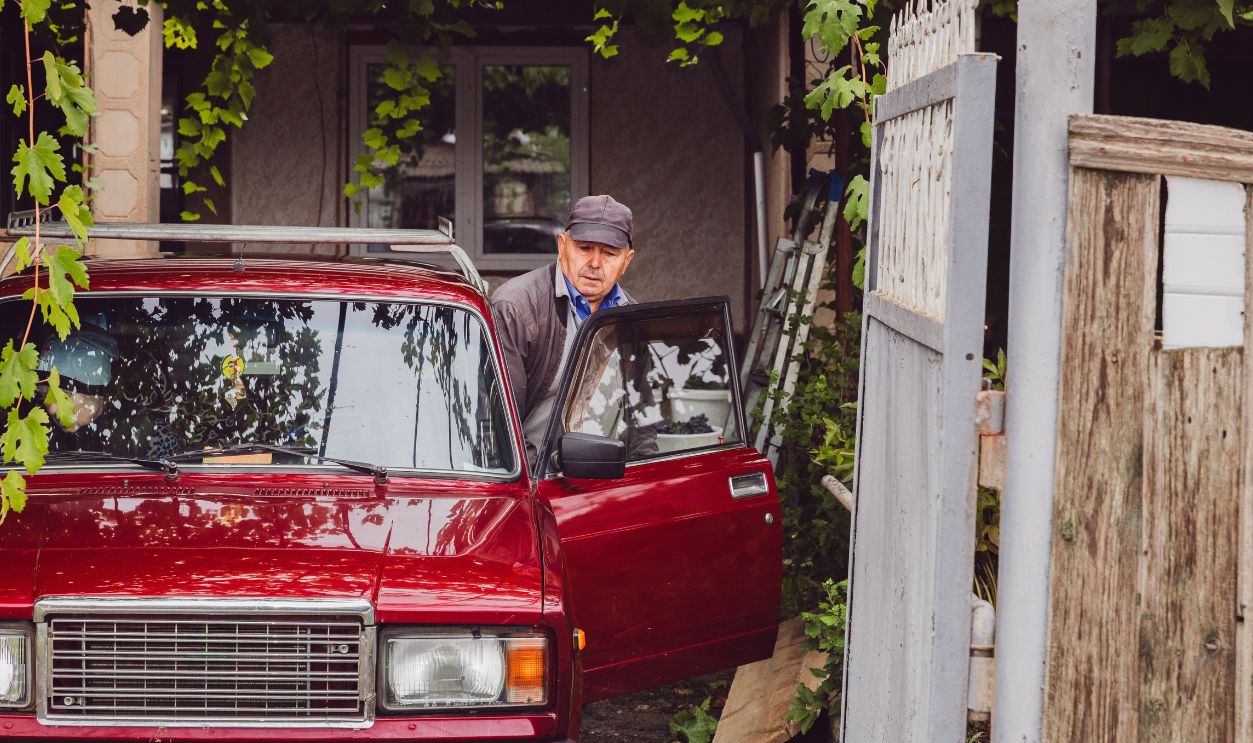A senior Caucasian male driver is preparing to get into an old-fashioned car.