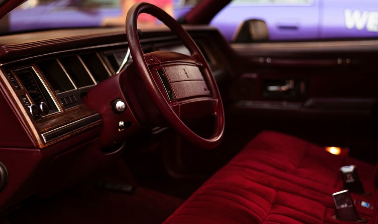 Close-up of a vintage car interior featuring plush red seats and a wooden dashboard