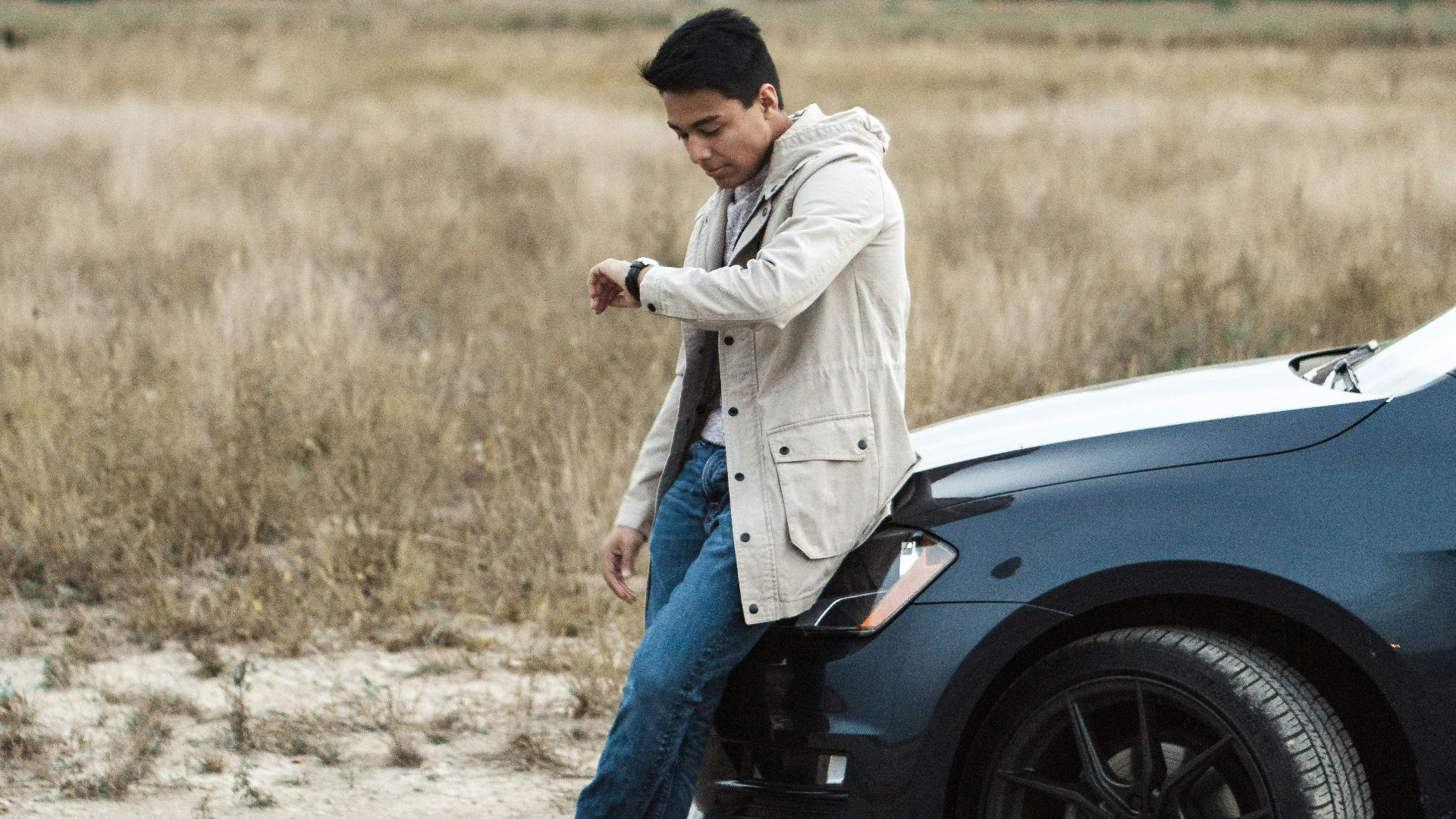 man sitting on car while looking at watch