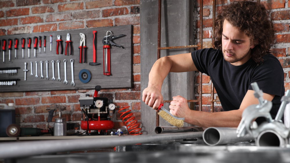 Man in home workshop garage work metal with handle wire brush.