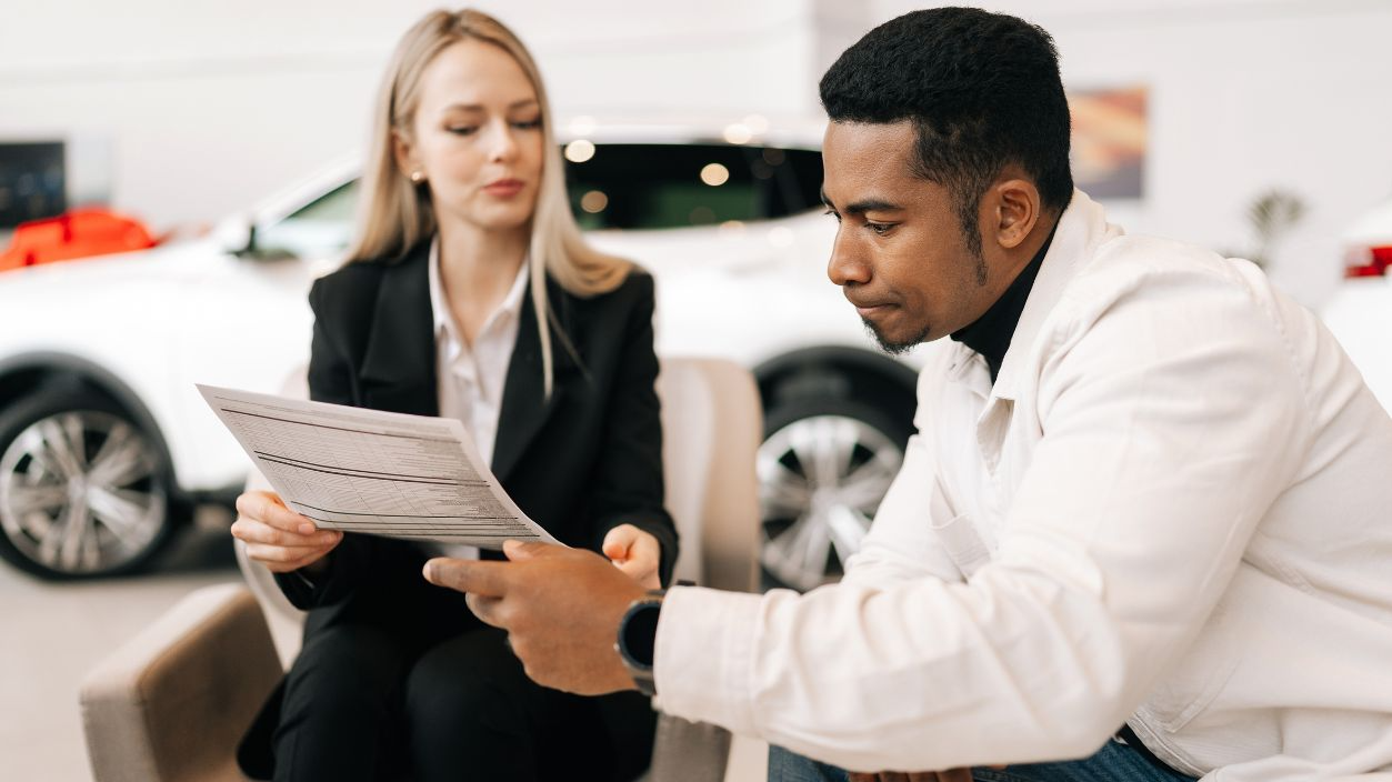Shutterstock-2556812455, Medium shot of female manager consulting doubtful black buyer, giving purchase agreement for review at showroom. Thoughtful African client receiving car purchase contract before signing in dealership