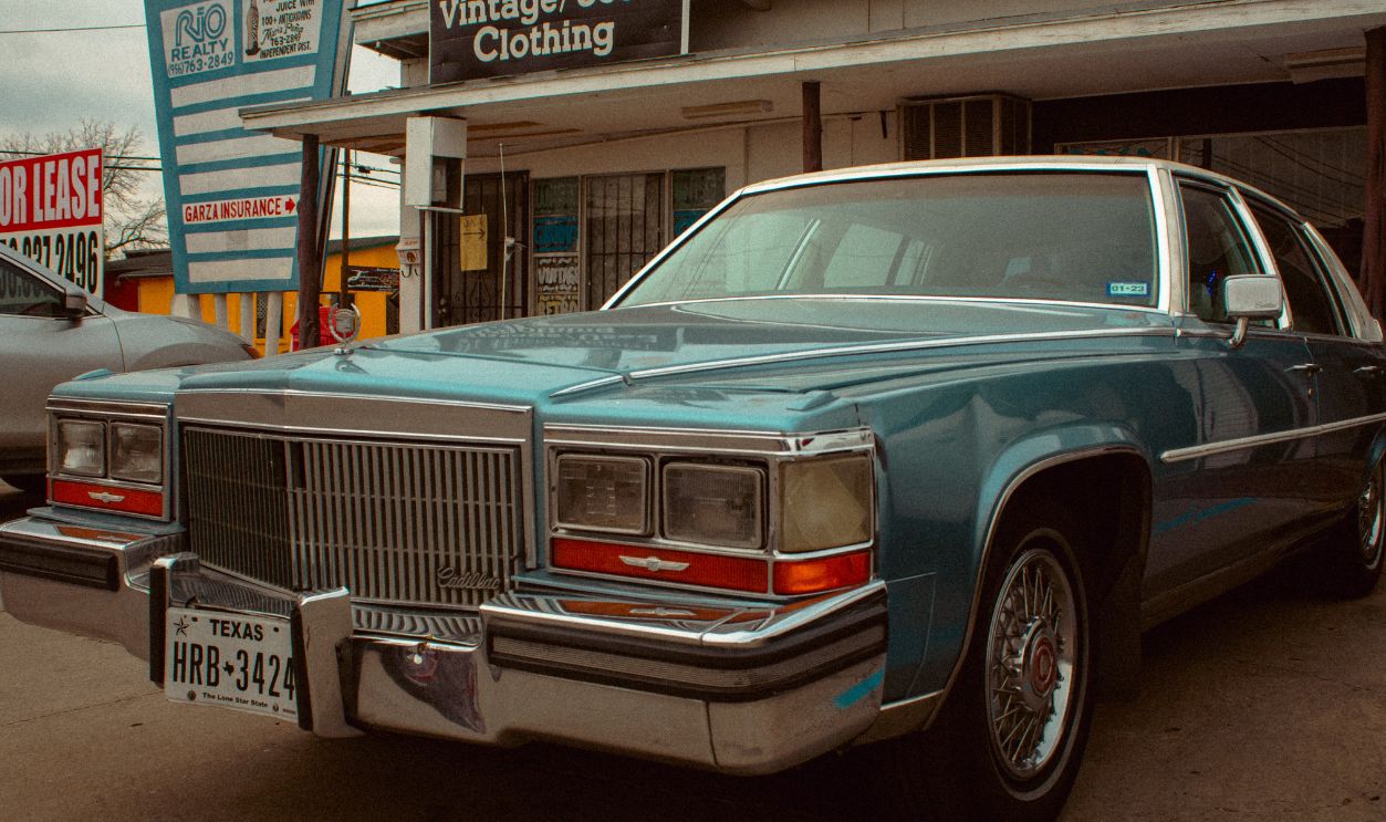 A vintage Cadillac parked outside a storefront under a cloudy sky, evoking nostalgia and classic urban charm