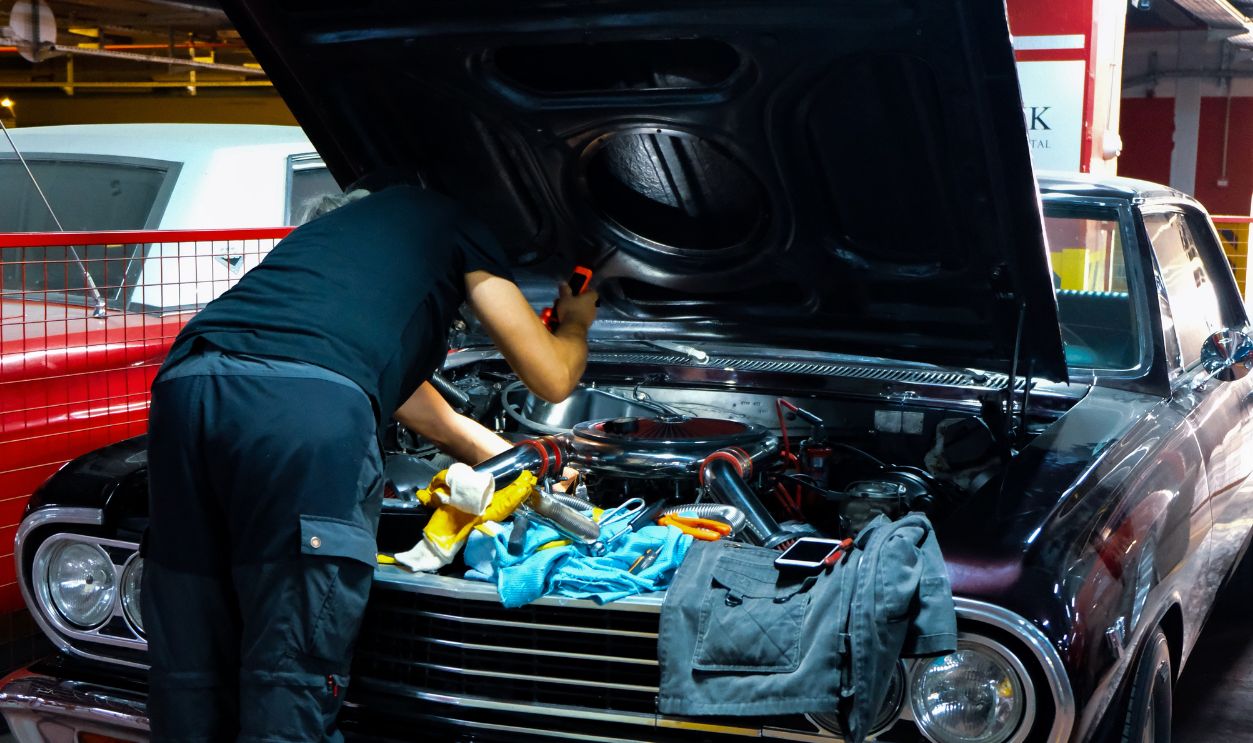 A mechanic works on a classic car engine in a dimly lit garage setting