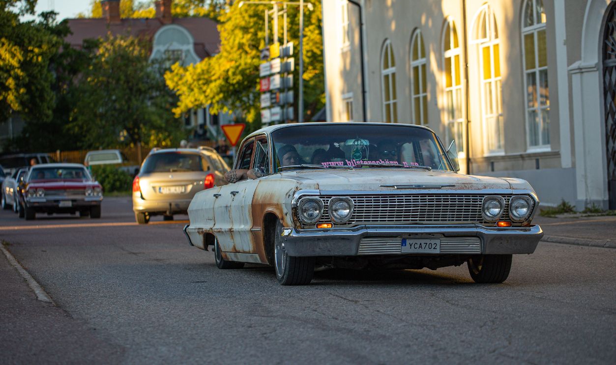 A classic rusty car cruising down a tranquil street with soft evening light