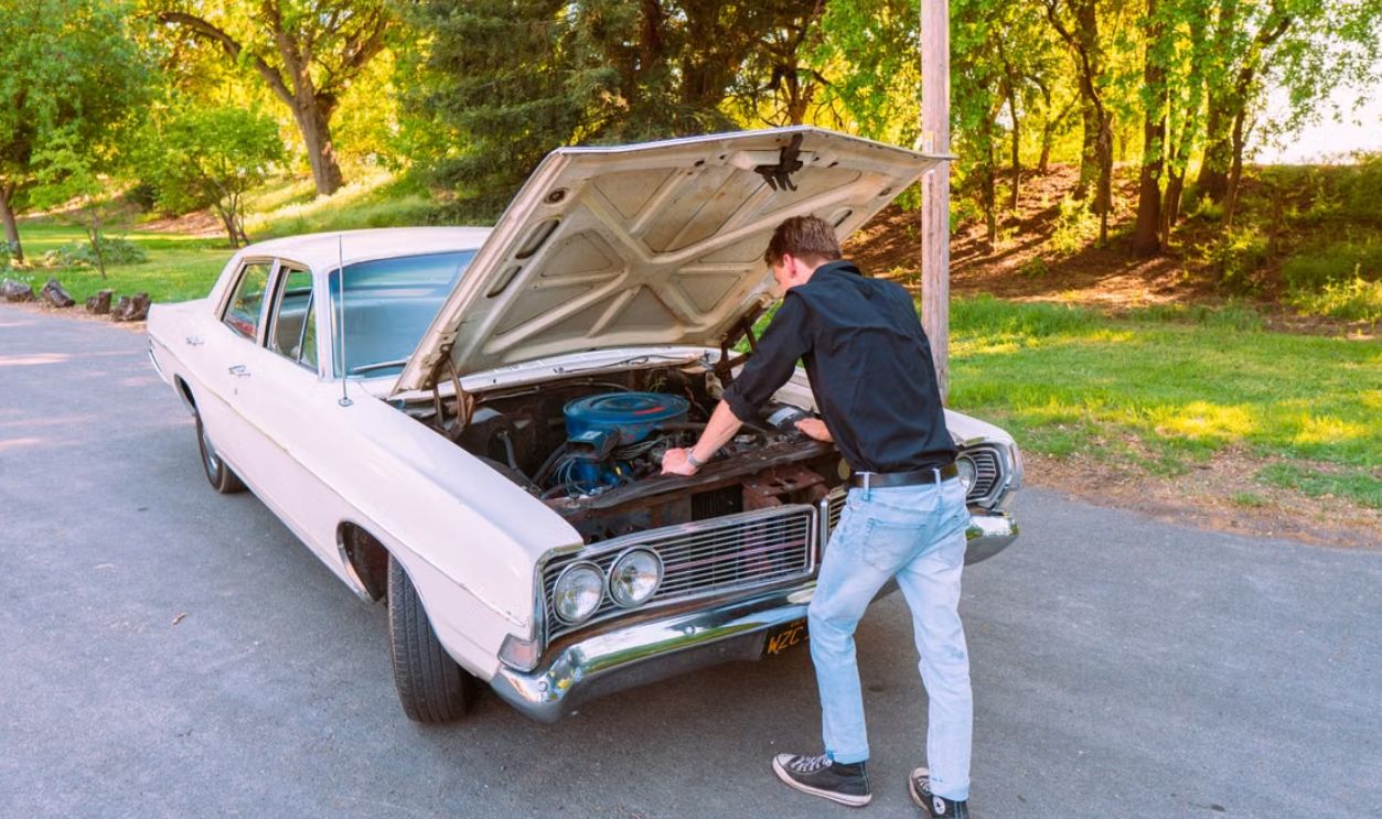 A man fixing a vintage car engine outdoors in Clarksburg, California, on a sunny day.