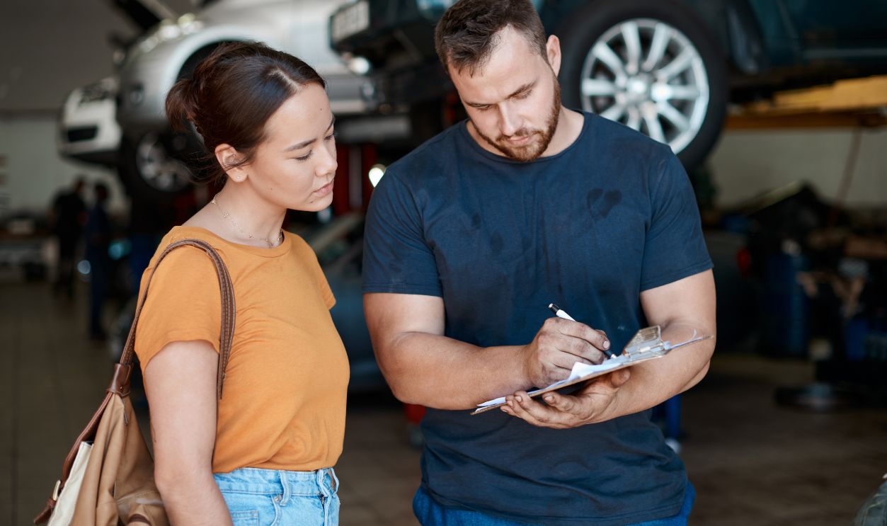 Shutterstock-2478227861, Woman, mechanic and sign paperwork in auto repair shop, invoice and service for car maintenance bill. Female person, clipboard and customer for vehicle transaction, contract and garage workshop
