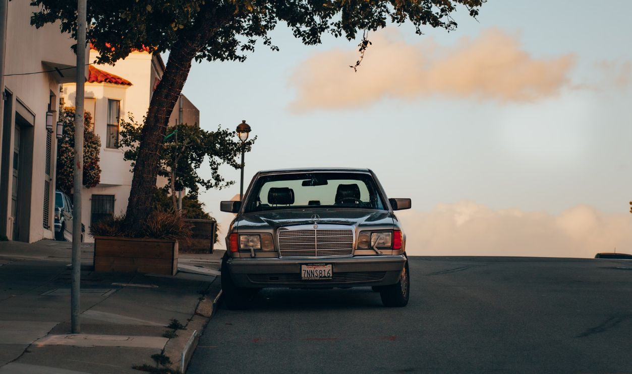 A classic Mercedes Benz parked on a serene street with tree shadows
