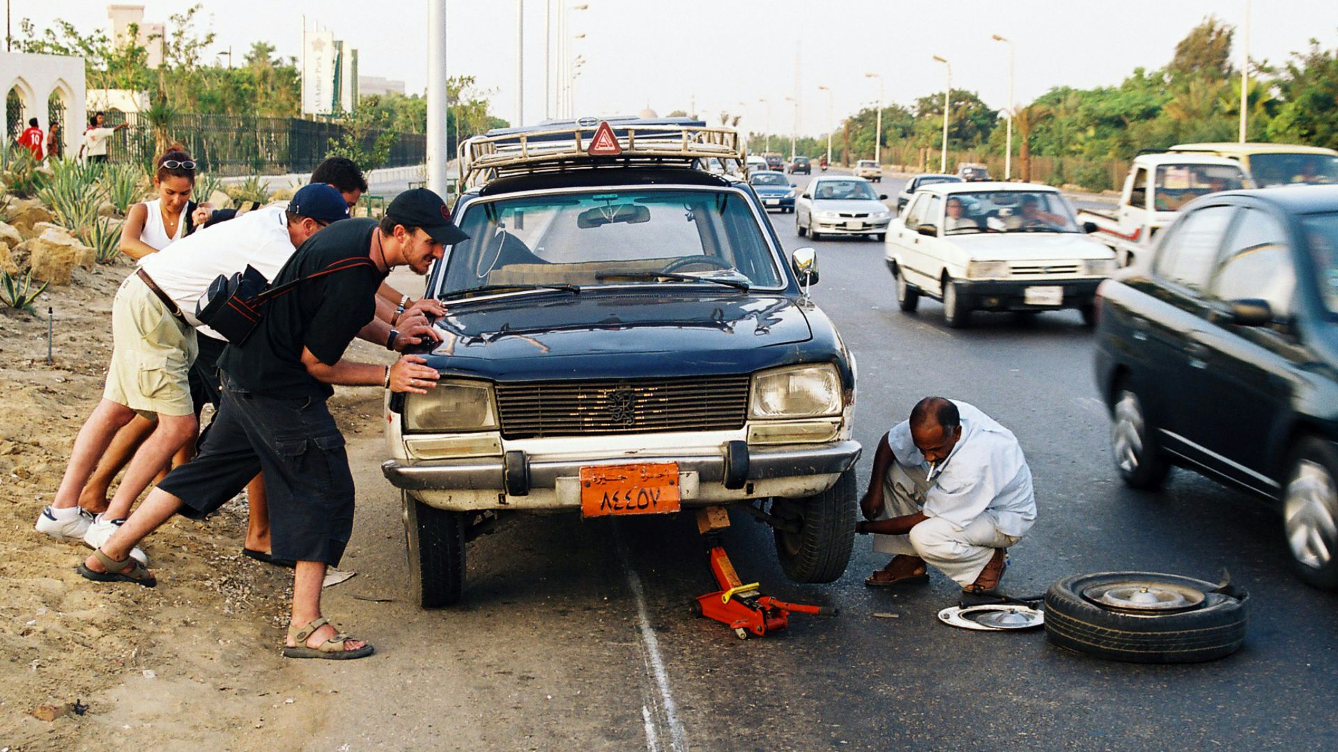 Men push a car while another changes its flat tire