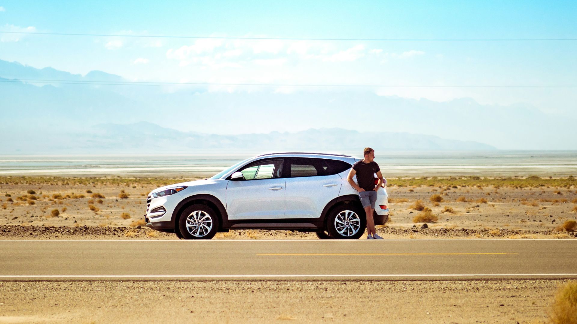 man standing beside white SUV near concrete road under blue sky at daytime