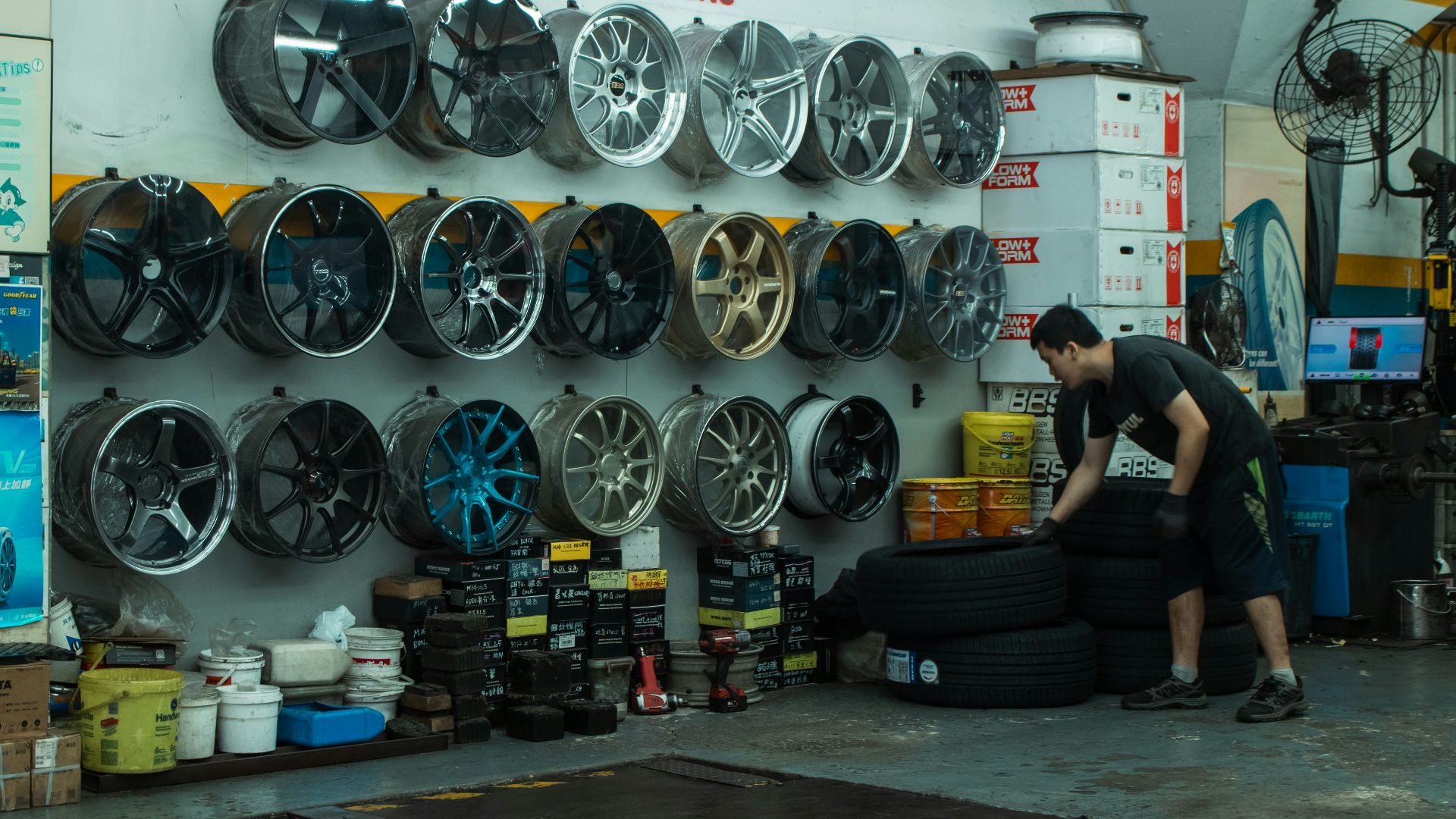 A person stacking tires in an auto shop with car wheels on the wall