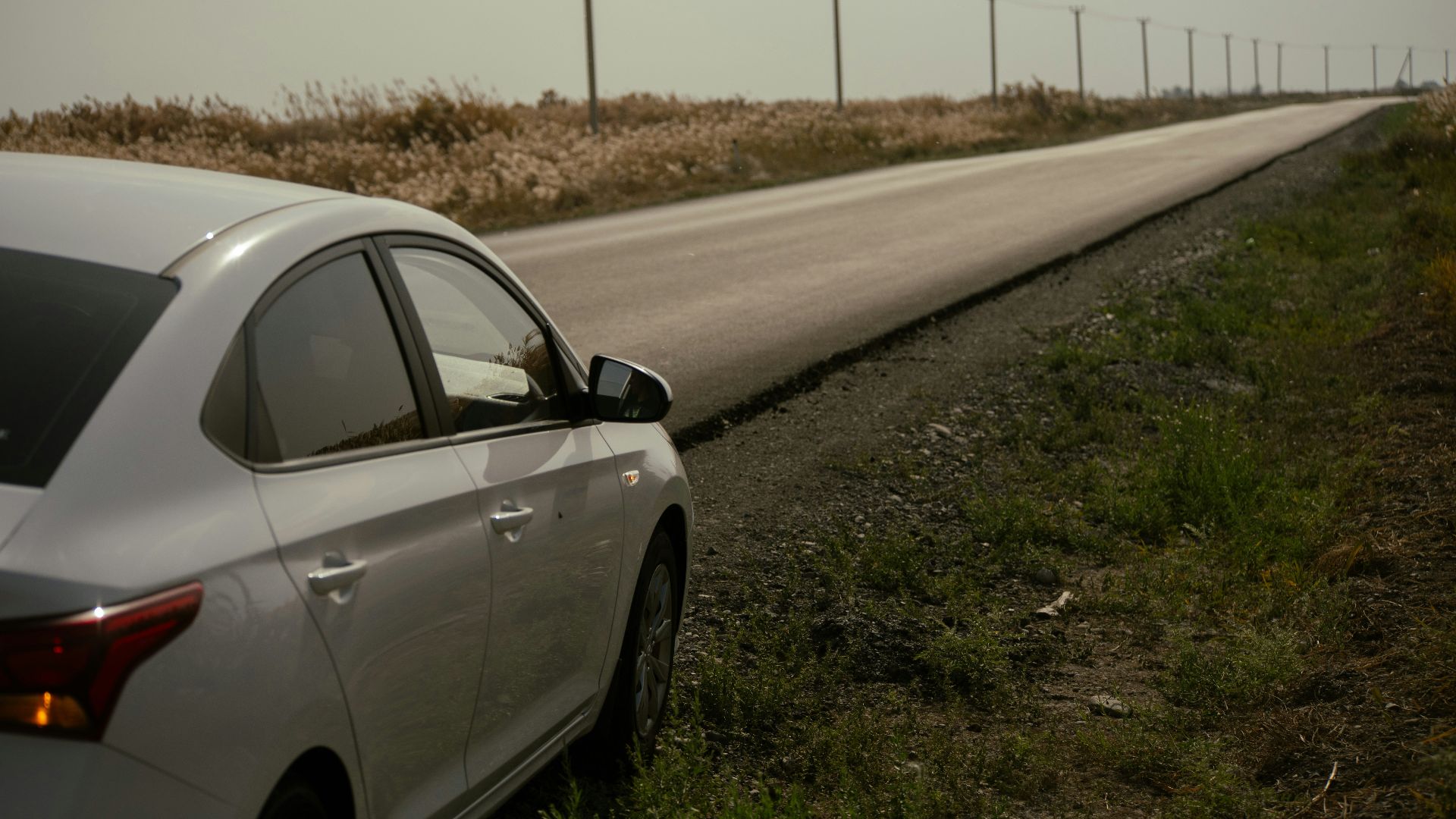 White car parked on the side of a long road