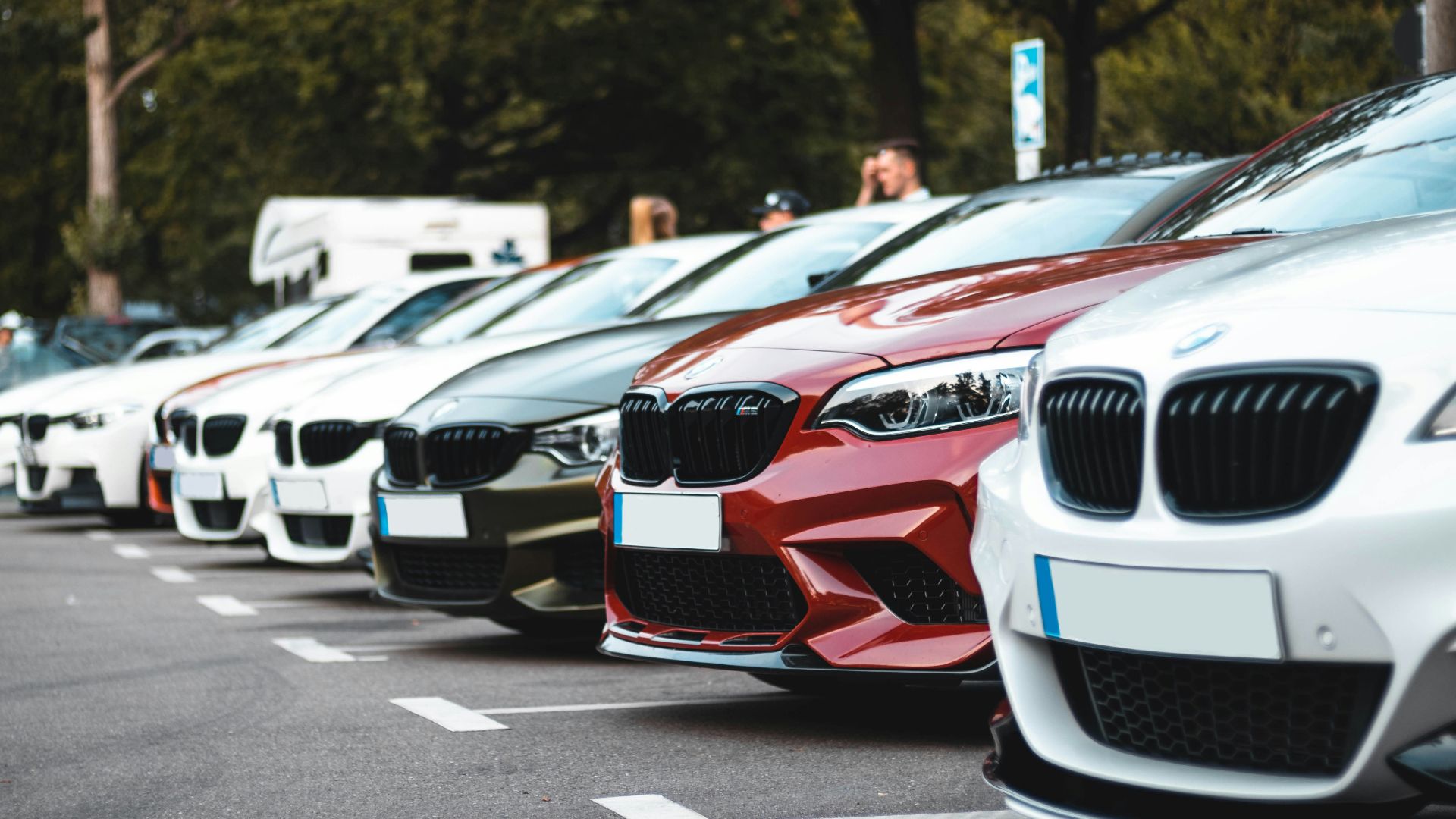 A row of parked cars including white, olive, and red sedans in a lot