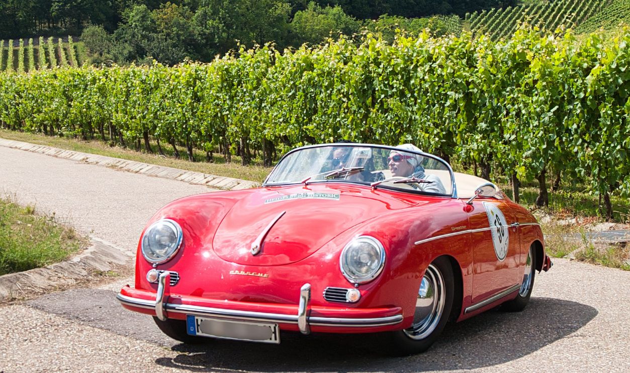 Classic red convertible sports car driving past a scenic vineyard with a castle backdrop